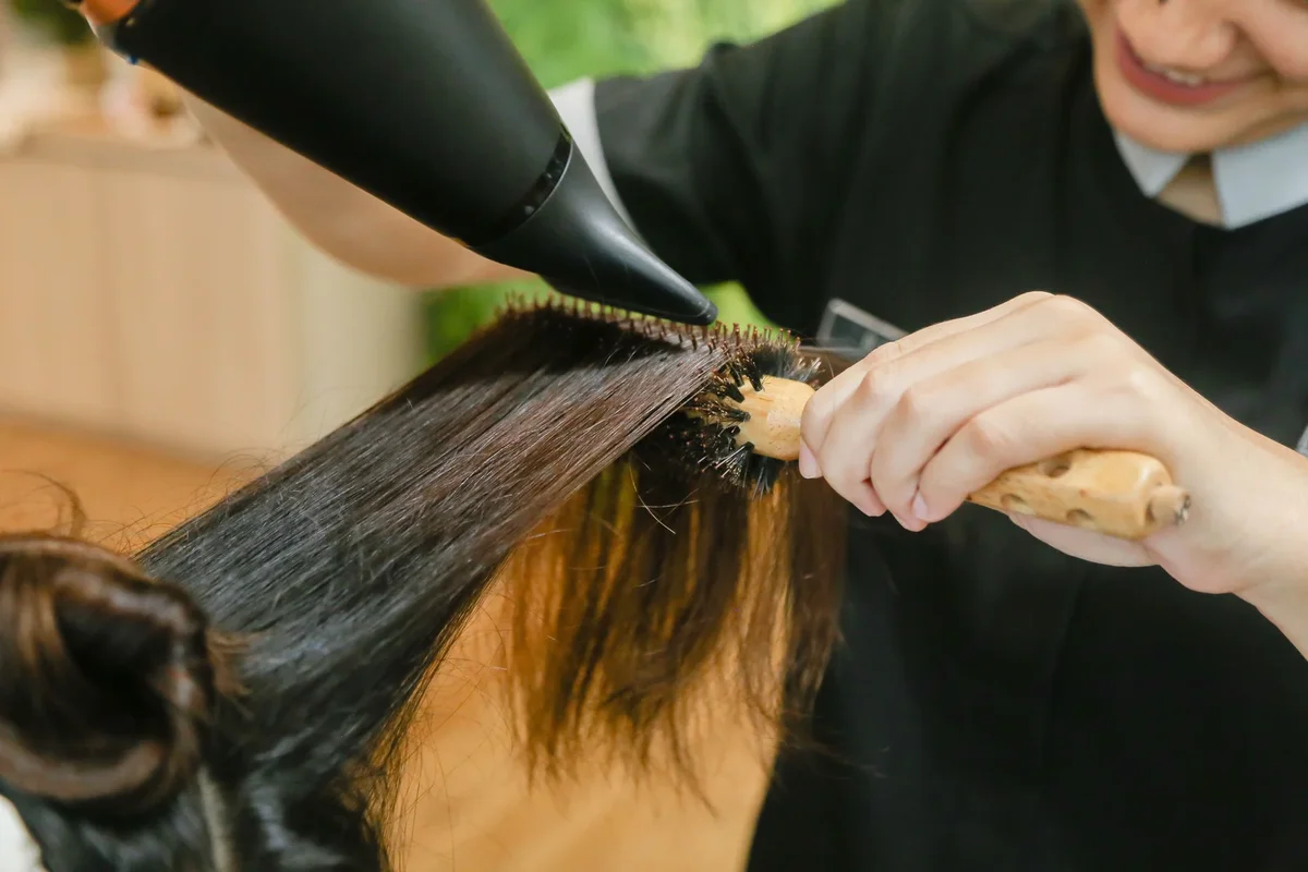 Femme utilisant une technique de brushing pour sécher ses cheveux avec un sèche-cheveux professionnel